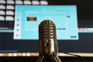 A close-up of a professional podcast microphone with a blurred computer screen in the background, ready for recording