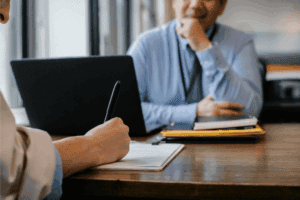 Professional interview or business meeting with candidate writing on a clipboard and interviewer listening across a desk